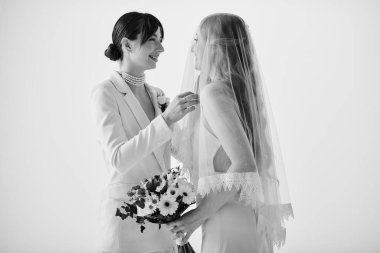 Two brides in white attire share a tender moment as they prepare for their wedding. The bride in the suit adjusts her partners veil. clipart