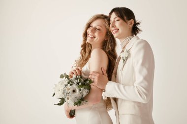 Beyaz düğün kıyafetli genç bir lezbiyen çift düğün törenlerinde kucaklaşır ve gülümserler..