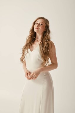 Beyaz gelinlikli güzel bir gelin beyaz bir arka planda duruyor, özel gününü kutlamaya hazır..