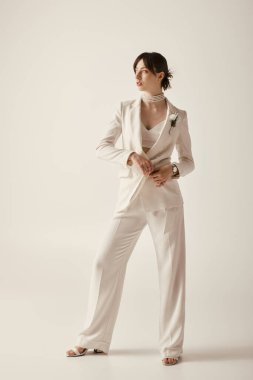 Güzel bir gelin beyaz bir arkaplanda beyaz bir takım elbise içinde poz verir..