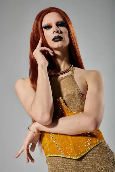 stock image A drag queen with long red hair and bold makeup poses in a shimmering gold outfit.