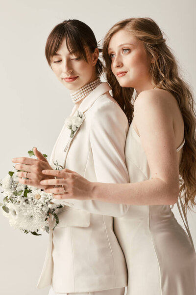 Two beautiful brides in white attire embrace during their wedding ceremony, a symbol of their love and commitment.