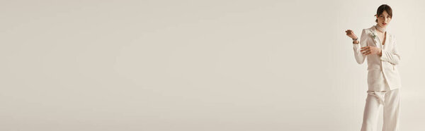 Красивая молодая невеста позирует в потрясающем белом свадебном костюме на белом фоне. Ее уверенная позиция и элегантный стиль демонстрируют современную свадебную моду.