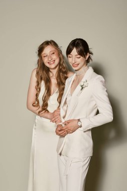 Beyaz düğün kıyafetli iki gelin birbirlerine yakın dururlar, düğün günlerinde neşeyle gülümserler..