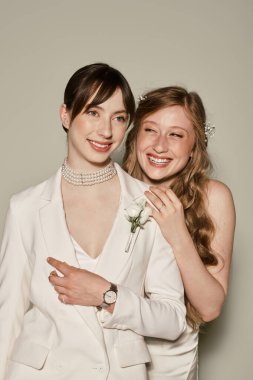 Two young women, dressed in white, celebrate their wedding day with a joyful embrace. clipart