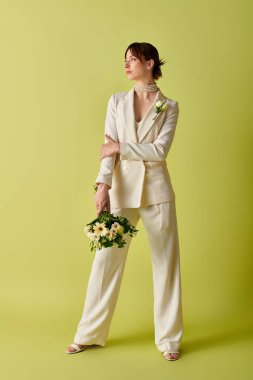 Beyaz takım elbiseli bir gelin elinde bir buket çiçekle yan tarafa bakar..