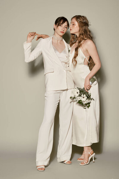 Two brides in white attire embrace on their wedding day, radiating love and happiness.