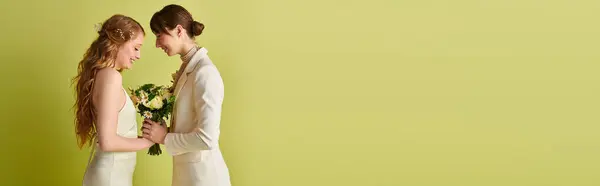 stock image Two brides in white wedding attire stand against a green background, holding a bouquet of flowers.