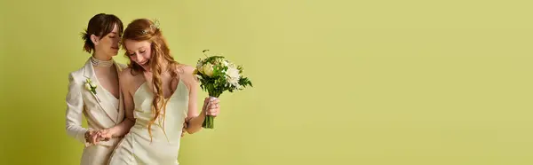 stock image Two young women, dressed in white wedding attire, stand together with one holding a bouquet. The couple smiles and enjoys their special day.