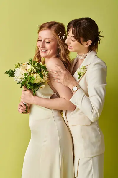 stock image Two brides in white wedding attire stand together, embracing, on a green backdrop.