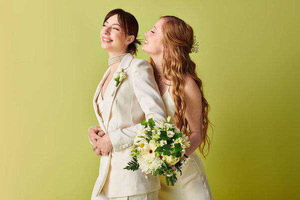 Две невесты в белом стоят спиной к спине, улыбаясь и держа букет цветов на зеленом фоне.