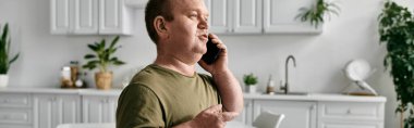 Modern bir mutfaktaki günlük kıyafetlerle telefonda konuşan bir adam..