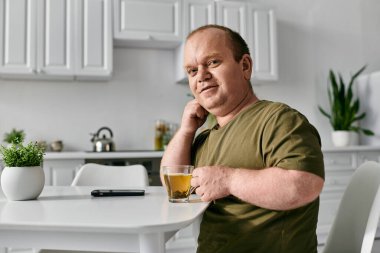 A man with inclusivity enjoys a cup of tea while sitting at a kitchen table. clipart