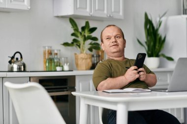 Günlük kıyafetleri olan bir adam mutfak masasına oturur ve akıllı telefon kullanır..