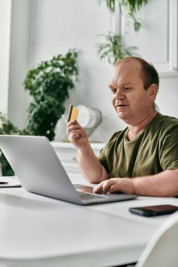 Kapsamlı bir adam elinde bir laptop ve kredi kartıyla masada oturuyor..
