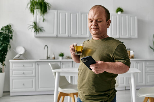 A man with inclusivity enjoys a cup of tea while checking his phone in his homes kitchen.