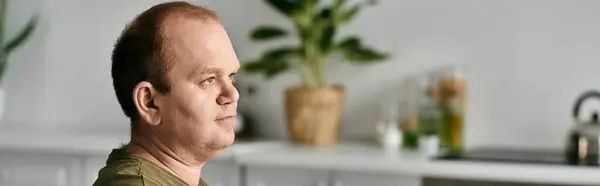 stock image A man with inclusivity sits in his kitchen, dressed casually, looking thoughtful.