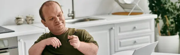 stock image A man with inclusivity relaxes in his home, enjoying a quiet moment in his kitchen.