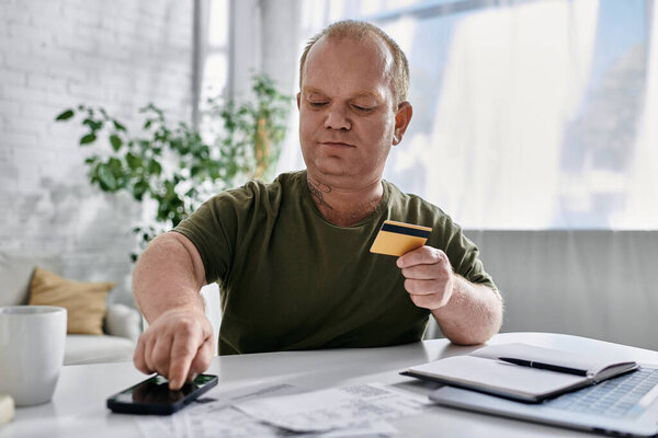 A man with inclusivity sits at a table in his home, making a payment with a credit card.