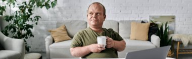 A man with inclusivity sits comfortably in his home, holding a mug, looking thoughtfully into the distance. clipart
