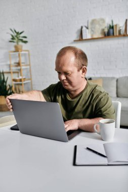Kapsamlı bir adam evindeki bir masada oturuyor ve laptopuyla uğraşıyor..