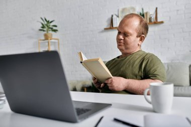 A man with inclusivity sits at a desk in his home, reading a book. clipart