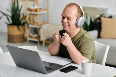 A man with inclusivity wearing headphones sits at a desk in his home office, working on a laptop. clipart