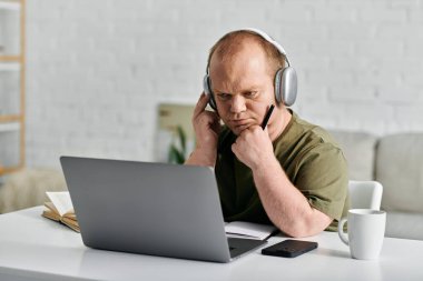 Masasında oturan, kulaklık takan, dizüstü bilgisayarına odaklanmış bir adam..