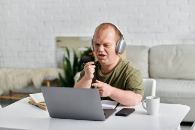 Günlük kıyafetleri olan bir adam evindeki bir masada oturup bilgisayarını ve kulaklıklarını kullanarak tutkulu bir online sohbete girişir..