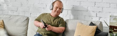 Kapsayıcı kulaklık takan bir adam evdeki koltukta oturup müzik dinler..