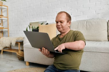 Kapsamlı bir adam evinde rastgele yerde oturuyor, dizüstü bilgisayarında interneti karıştırıyor..