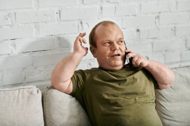 Kapsayıcı giyinmiş bir adam kanepede oturur ve telefonda konuşur..