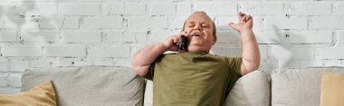 Kapsamlı giyinmiş bir adam evde telefonla konuşurken gülümsüyor..