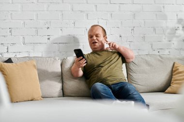 Kapsayıcılığı olan bir adam koltukta rahat rahat giyinir ve telefonunu kullanır..