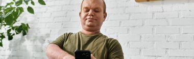 Kapsamlı giyinmiş, evinde oturan ve akıllı telefonunu kullanan bir adam..