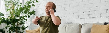 A man with inclusivity sits on a couch in his home, casually dressed and speaking on the phone. clipart