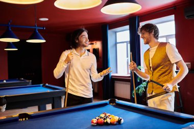 Arkadaşlar bilardo masasının başında durup, bilardo oynamadan önce güler ve konuşurlar..
