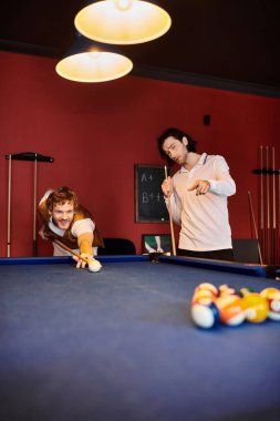 Arkadaşlar normal ortamlarda bilardo oynarlar, biri atış yaparken diğeri dikkatle izler..