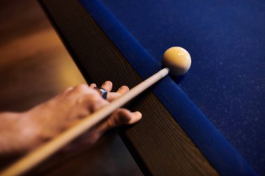 Bilardo ıstakası tutan bir elin yakın çekimi, keçeli masanın üzerindeki beyaz topa nişan alınmıştı..