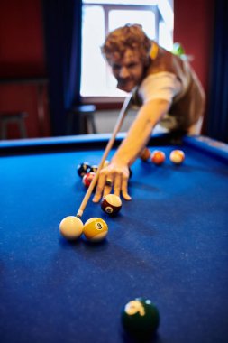 Bir adam bilardo oynuyor, atış yapmaya odaklanmış..