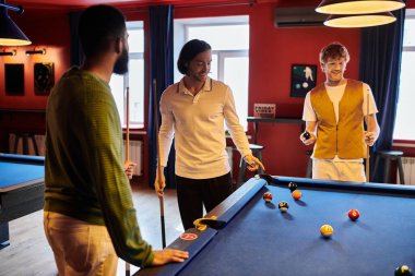 Arkadaşlar loş bir odada rastgele giyinmiş bilardo oynuyorlar..