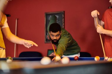 Arkadaşlar bilardo oynar. Dikkatlice atışına odaklanır..