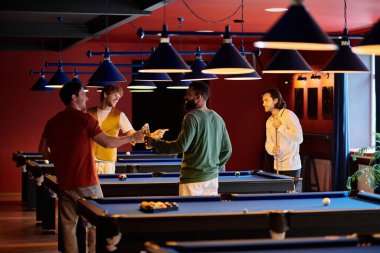 Arkadaşlar, mavi bilardo masaları ve kırmızı duvarları olan parlak ışıklı bir odada bilardo oynarlar..