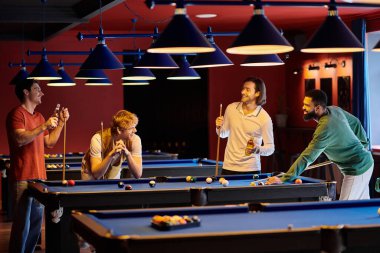 Gündelik giysiler içindeki arkadaşlar bilardo oynamak için bilardo masasının etrafında toplandılar..