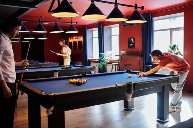 Friends enjoying a game of billiards in a dimly lit bar. clipart