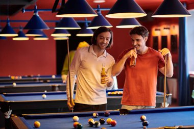 Friends play pool in a dimly lit room, enjoying drinks and each others company. clipart