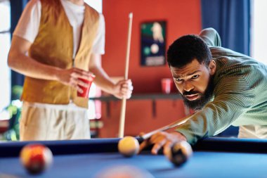 Bir adam atışını bilardo masasında yapmaya odaklanır. Etrafı arkadaşlarıyla çevrilidir..