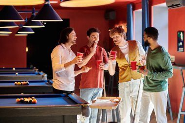 Arkadaşlar bir bilardo masasının etrafında durur, içkiler el ele, sıradan bir ortamda..