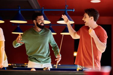 Arkadaşlar bilardo salonundaki zaferi kutluyorlar, biri zafer için elini kaldırıyor, diğeri ıstakasını neşeli bir ifadeyle tutuyor..