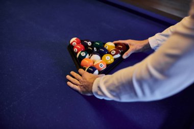 Bir oyuncu bilardo toplarını keçeli masada bir üçgene yerleştirir, arkadaşlarıyla sıradan bir oyuna hazırlanır..